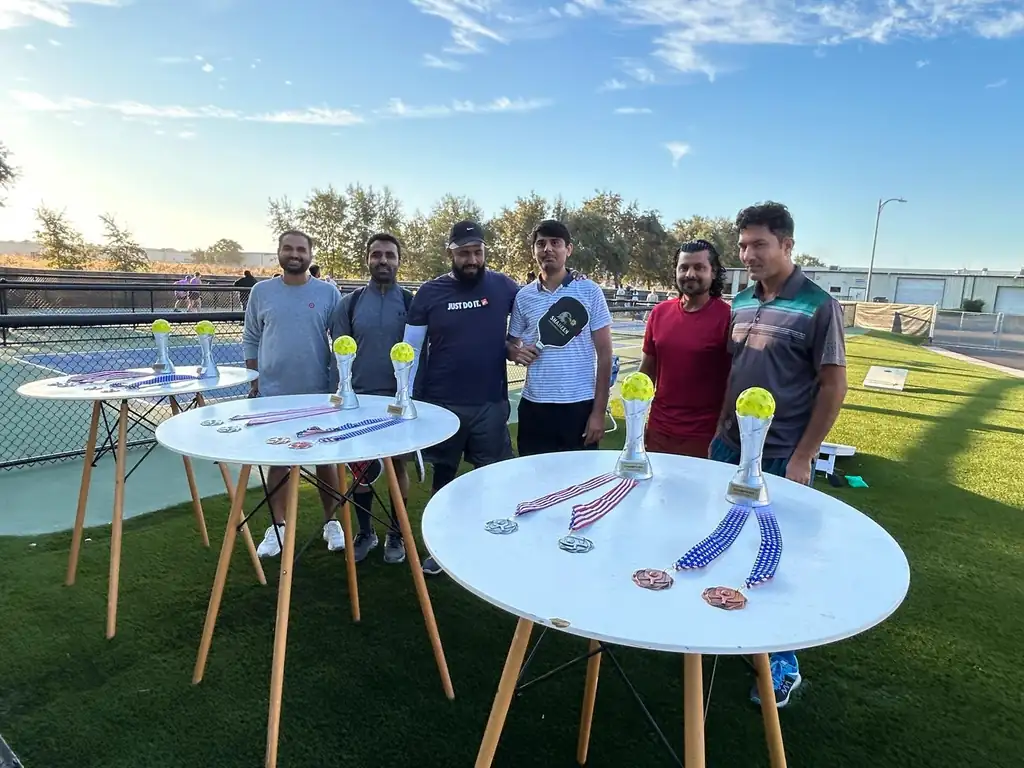 Shaheen Pickleball Club members gathered behind tables of trophies and medals at the courts